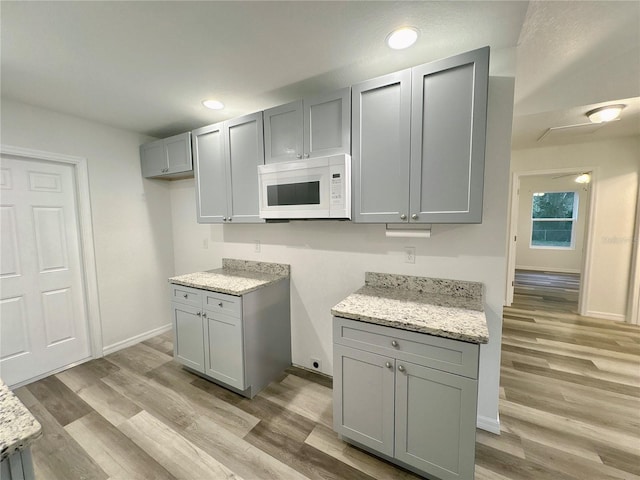 kitchen with light stone counters, gray cabinets, and light hardwood / wood-style flooring