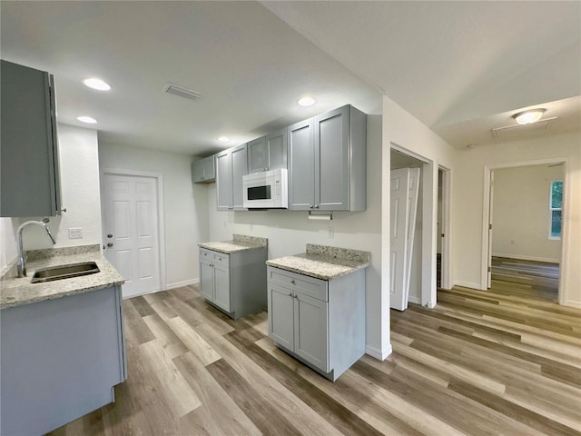 kitchen featuring light stone counters, sink, gray cabinets, and light hardwood / wood-style floors