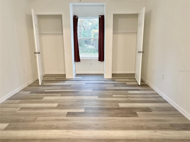 unfurnished bedroom featuring multiple closets and light hardwood / wood-style flooring