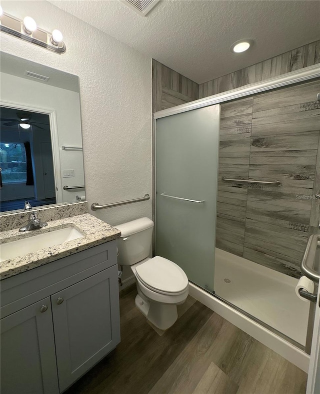 bathroom featuring wood-type flooring, vanity, an enclosed shower, toilet, and a textured ceiling