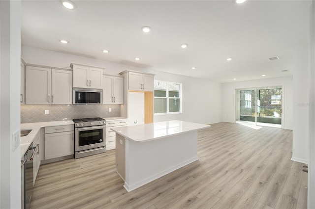 kitchen featuring a center island, light wood-type flooring, backsplash, stainless steel appliances, and white cabinets