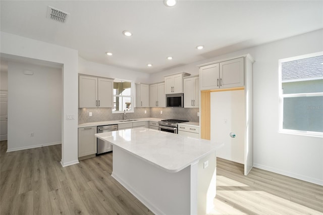 kitchen featuring appliances with stainless steel finishes, tasteful backsplash, sink, a center island, and light hardwood / wood-style flooring