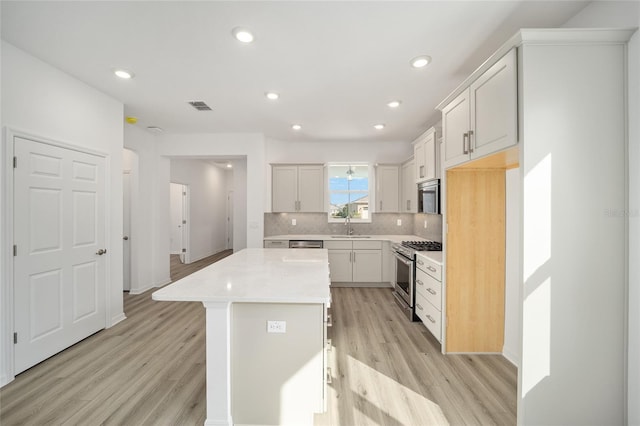 kitchen featuring sink, tasteful backsplash, high end stainless steel range, white cabinets, and a kitchen island