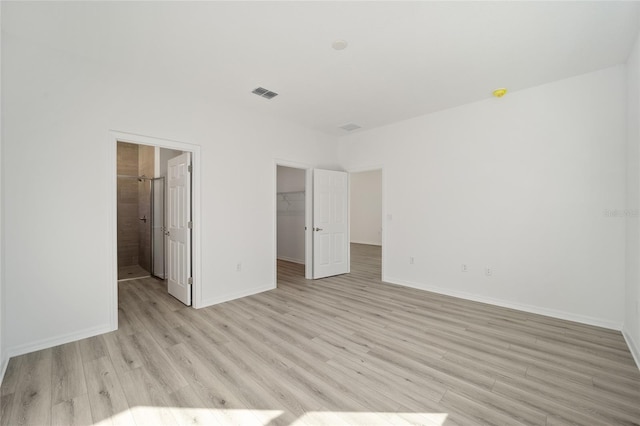 unfurnished bedroom featuring connected bathroom, a spacious closet, light hardwood / wood-style flooring, and a closet