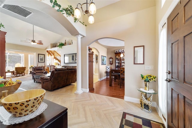 entrance foyer featuring lofted ceiling, ceiling fan with notable chandelier, light parquet floors, and ornate columns