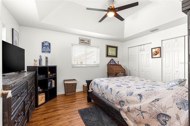 bedroom featuring hardwood / wood-style flooring, two closets, ceiling fan, and a tray ceiling