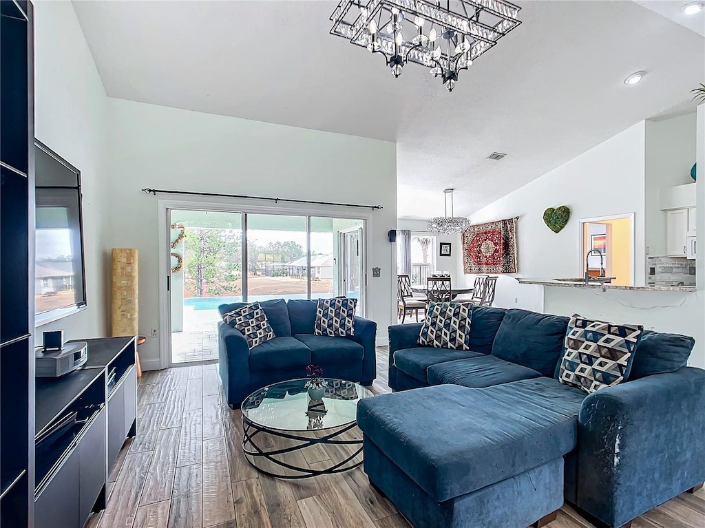 living room with an inviting chandelier, sink, lofted ceiling, and light wood-type flooring