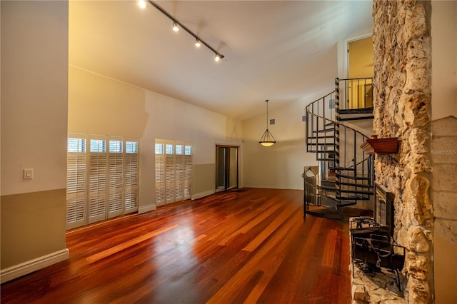 interior space featuring a high ceiling, wood-type flooring, a stone fireplace, and track lighting