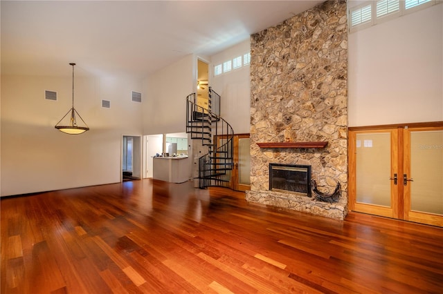 unfurnished living room featuring french doors, a towering ceiling, a fireplace, and hardwood / wood-style floors