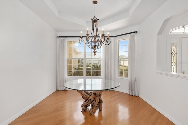 dining area featuring a notable chandelier, a tray ceiling, and wood-type flooring