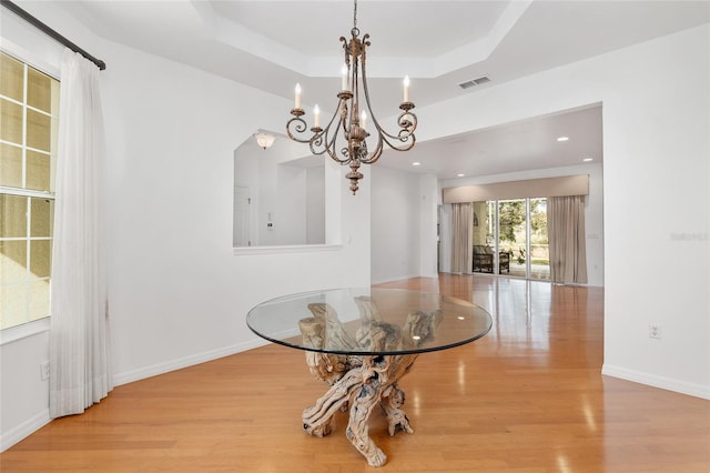 dining area featuring a tray ceiling, light hardwood / wood-style flooring, and a notable chandelier