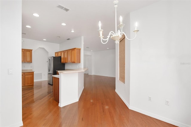 kitchen featuring an inviting chandelier, kitchen peninsula, stainless steel refrigerator, and light hardwood / wood-style floors