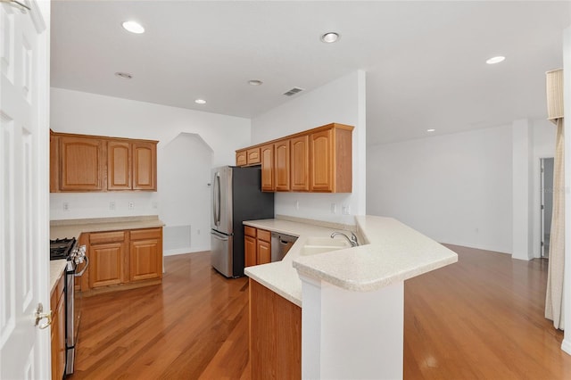 kitchen featuring stainless steel appliances, sink, light wood-type flooring, and kitchen peninsula