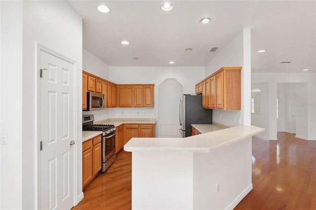 kitchen with appliances with stainless steel finishes, kitchen peninsula, and light hardwood / wood-style floors