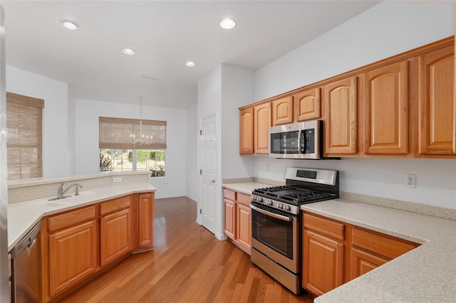 kitchen with pendant lighting, sink, stainless steel appliances, light hardwood / wood-style floors, and a chandelier