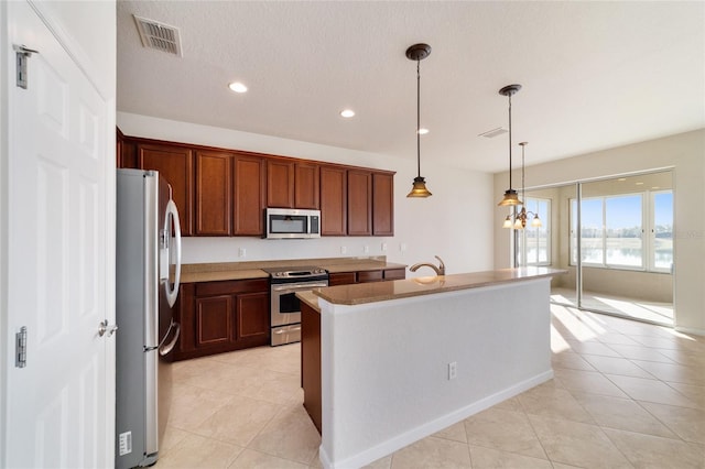 kitchen with light tile patterned flooring, decorative light fixtures, a center island with sink, a textured ceiling, and stainless steel appliances