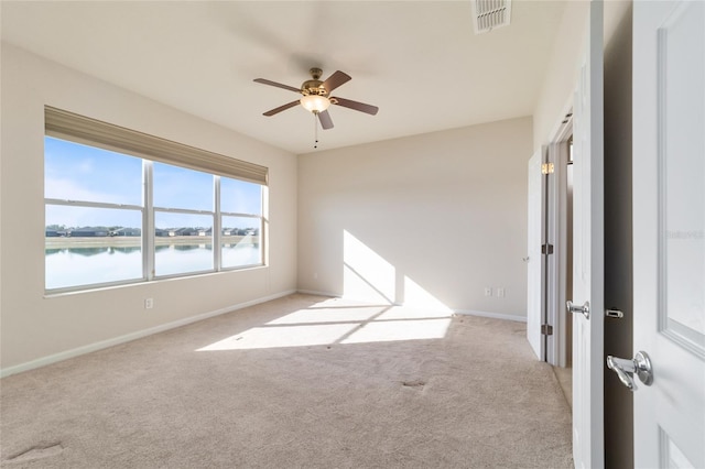 spare room with a water view, light carpet, and ceiling fan