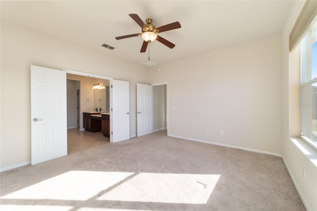 unfurnished bedroom featuring light carpet, ensuite bath, and ceiling fan