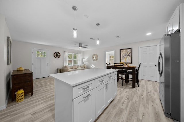 kitchen featuring stainless steel refrigerator, white cabinetry, light hardwood / wood-style floors, and hanging light fixtures