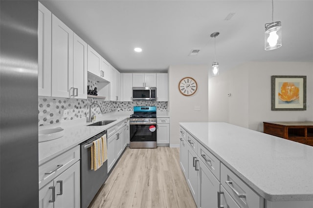 kitchen with sink, tasteful backsplash, decorative light fixtures, stainless steel appliances, and white cabinets