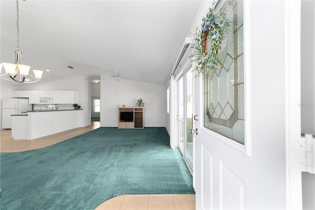 unfurnished living room featuring vaulted ceiling, ceiling fan with notable chandelier, light carpet, and a textured ceiling