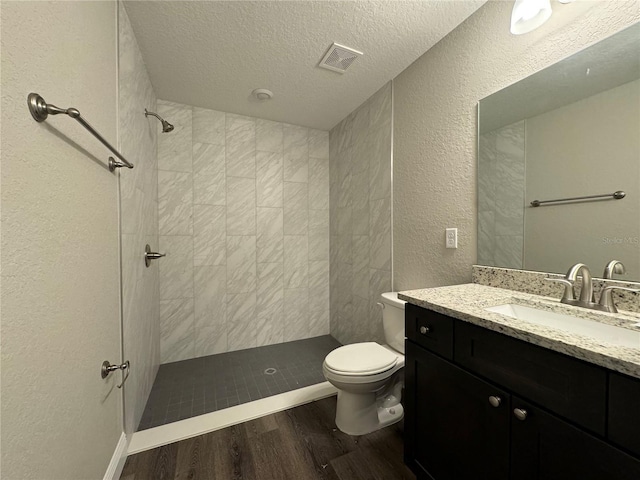 bathroom with a tile shower, hardwood / wood-style flooring, vanity, toilet, and a textured ceiling