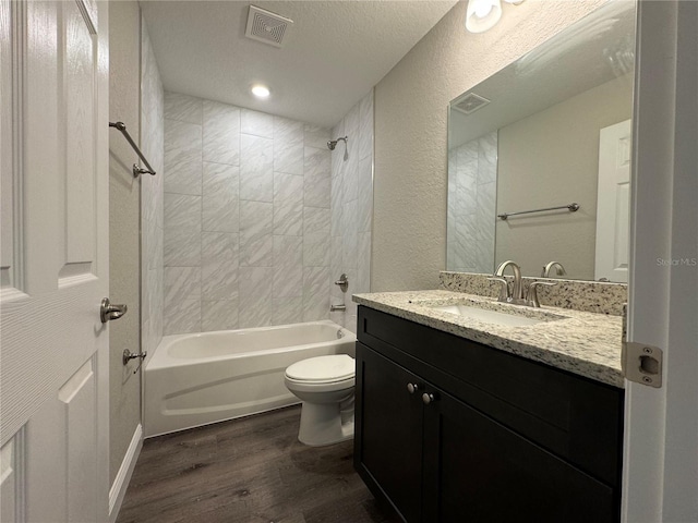 full bathroom featuring hardwood / wood-style flooring, vanity, a textured ceiling, tiled shower / bath, and toilet