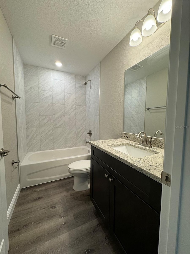 full bathroom featuring tiled shower / bath, hardwood / wood-style flooring, vanity, toilet, and a textured ceiling