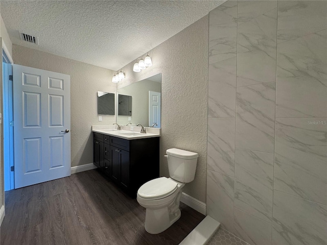 full bathroom featuring wood finished floors, visible vents, a textured ceiling, toilet, and a textured wall