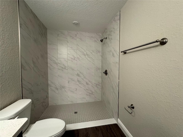 full bath with toilet, a textured wall, tiled shower, wood finished floors, and a textured ceiling