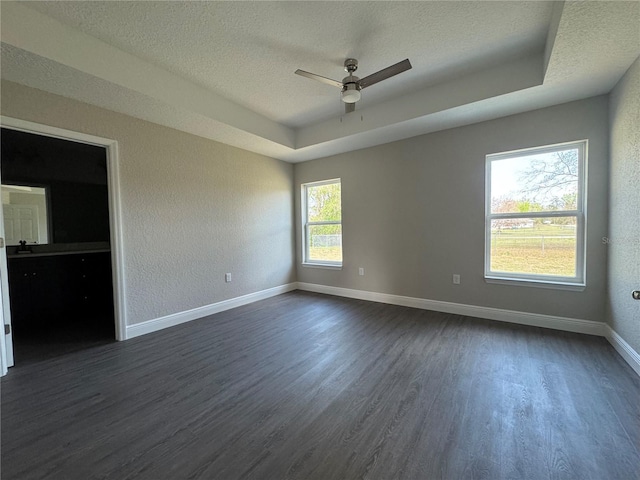 unfurnished room with a raised ceiling, baseboards, dark wood-type flooring, and a textured ceiling