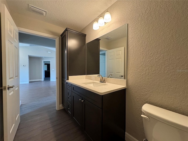 bathroom featuring wood finished floors, visible vents, a textured ceiling, toilet, and a textured wall