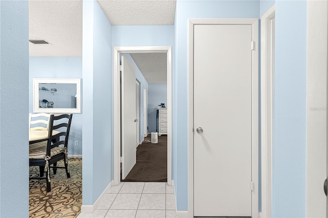 hallway with a textured ceiling and light tile patterned floors