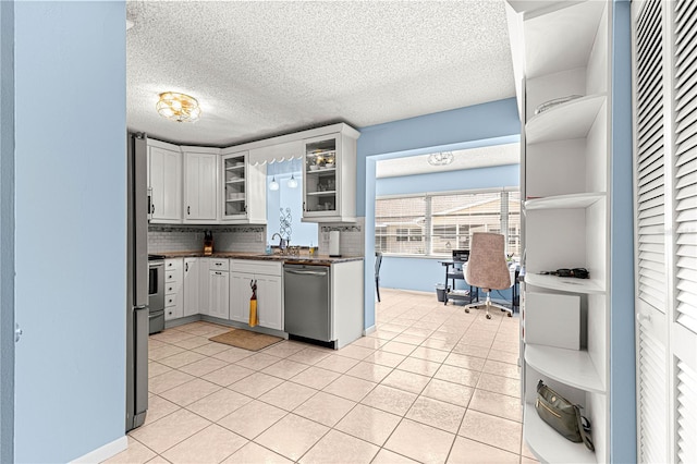 kitchen with light tile patterned floors, white cabinetry, backsplash, stainless steel appliances, and a textured ceiling