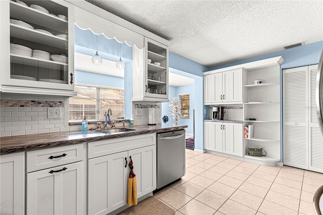 kitchen featuring sink, light tile patterned floors, dark stone countertops, dishwasher, and white cabinets