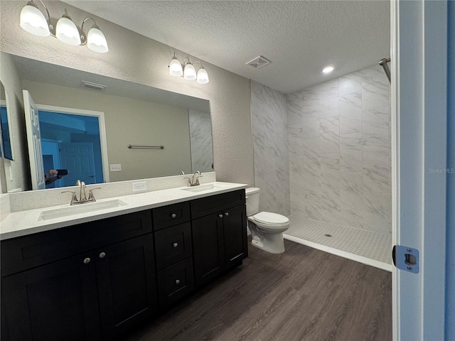 bathroom with visible vents, a sink, a textured ceiling, wood finished floors, and a textured wall