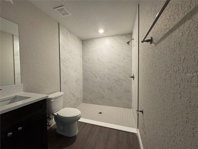 full bath featuring wood finished floors, a shower stall, a textured ceiling, toilet, and a textured wall