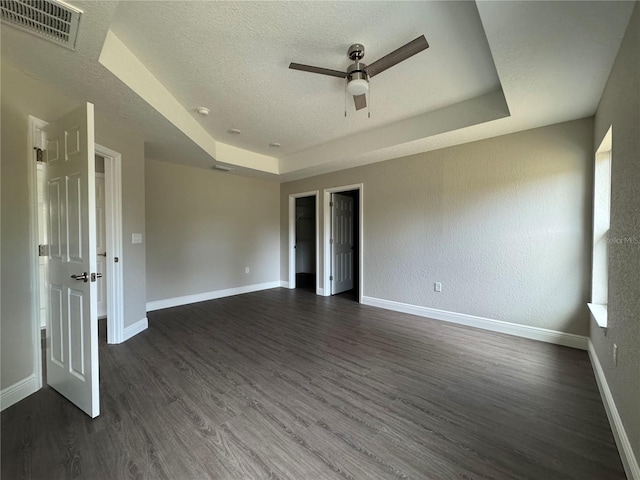 empty room featuring a tray ceiling, baseboards, visible vents, and dark wood-style flooring