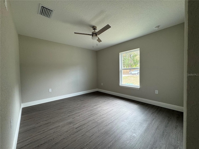 spare room featuring visible vents, a ceiling fan, dark wood-type flooring, and baseboards