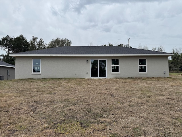 back of house featuring central AC unit, a shingled roof, and a yard