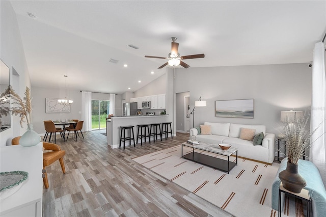 living room with high vaulted ceiling, ceiling fan with notable chandelier, and light hardwood / wood-style floors