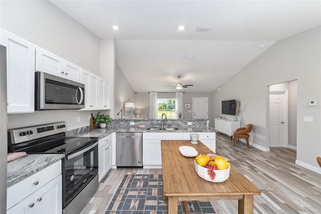 kitchen with lofted ceiling, sink, appliances with stainless steel finishes, white cabinetry, and kitchen peninsula