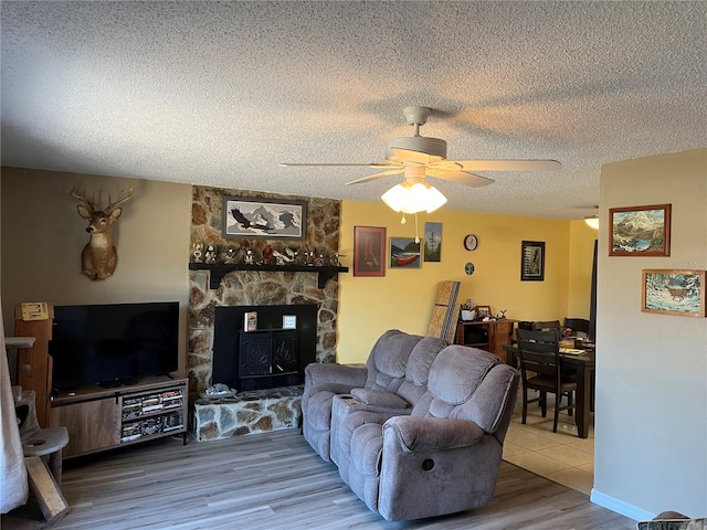 living room with hardwood / wood-style flooring, ceiling fan, a fireplace, and a textured ceiling