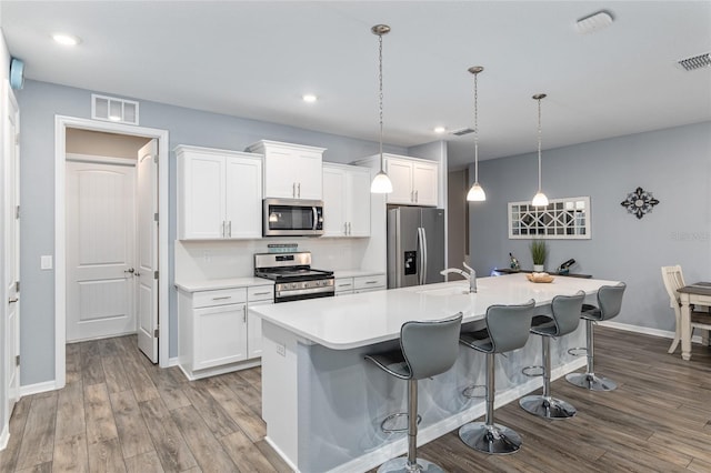 kitchen with appliances with stainless steel finishes, a kitchen breakfast bar, an island with sink, and white cabinets