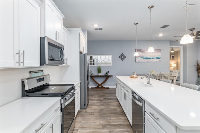 kitchen with decorative light fixtures, white cabinetry, sink, stainless steel appliances, and a center island with sink