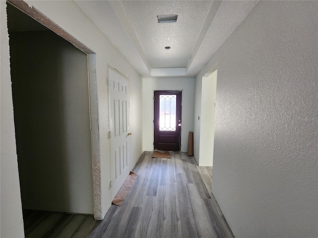 doorway featuring wood finished floors, a textured wall, a tray ceiling, and a textured ceiling