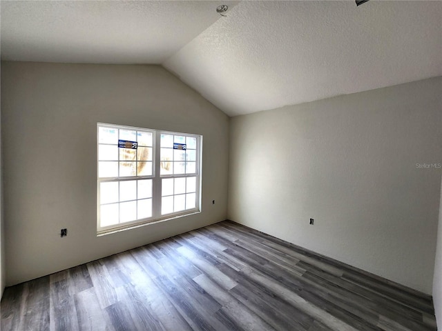 empty room featuring a textured ceiling, wood finished floors, and vaulted ceiling