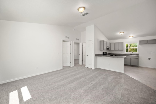 kitchen featuring gray cabinets, vaulted ceiling, sink, light colored carpet, and kitchen peninsula