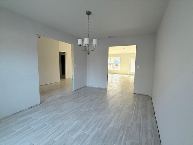 spare room featuring a notable chandelier and light wood-type flooring