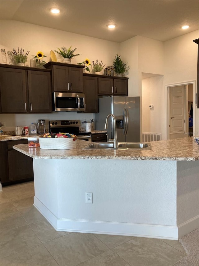 kitchen with sink, light tile patterned floors, appliances with stainless steel finishes, dark brown cabinetry, and light stone countertops